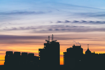 Obraz premium Cityscape with wonderful varicolored vivid dawn. Amazing dramatic blue sky with purple and violet clouds above dark silhouettes of city buildings. Atmospheric background of orange sunrise. Copy space.