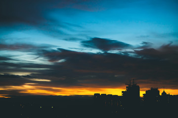 Cityscape with wonderful varicolored vivid dawn. Amazing dramatic blue cloudy sky above dark...