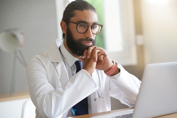 Portrait of male doctor sitting in front of laptop computer
