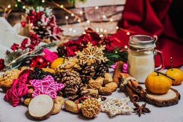 Christmas and new year celebration table decoration background with garland, toys, cookies, cinnamon, pine cones, wallnuts and candle in cup