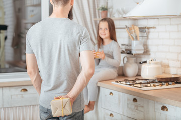 dad hiding present for daughter behind his back. holiday suprise gift for a child.