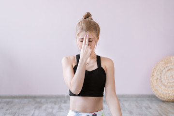 Front view portrait of beautiful young woman wearing white tank top working out against grey wall, resting after doing yoga exercises, using nadi shodhana pranayama technique. Full length - obrazy, fototapety, plakaty