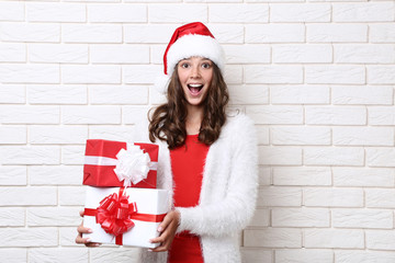 Surprised girl in santa hat holding gift boxes on brick wall background