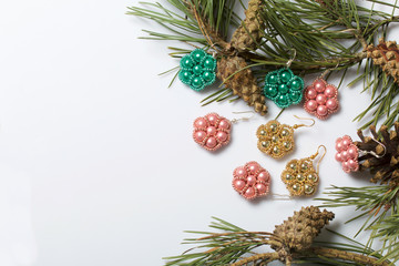 Women's earrings from beads among pine branches with cones. On a white background.