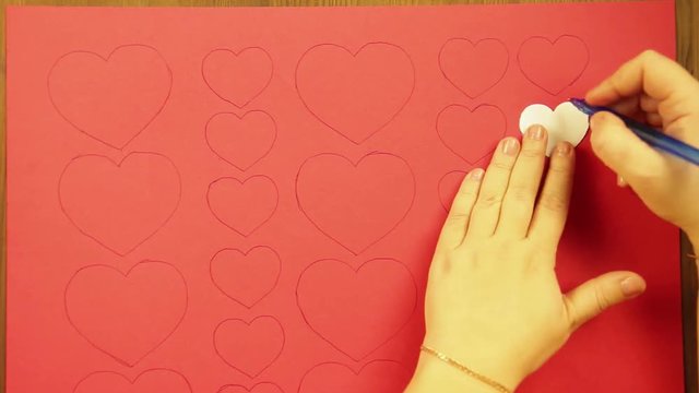 The girl draws on a red cardboard hearts of different sizes. Time laps