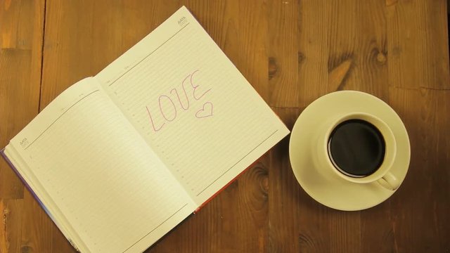 The girl writes in the diary the word love with a pink felt-tip pen and drinks coffee. Time laps