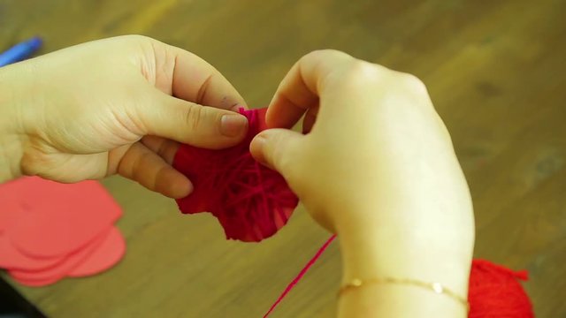 The girl makes a suverner from a red heart of cardboard and thread. Time laps