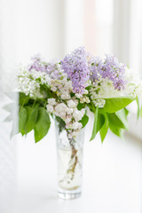 Lilac flowers in glass vase on window sill. Natural spring background with white and violet flowers.