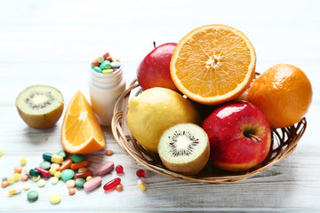 Ripe fruits in basket and colorful pills on wooden table