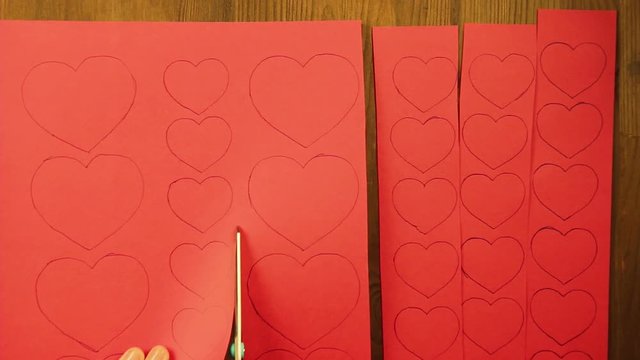 The girl cuts blanks of hearts from red cardboard. Close-up