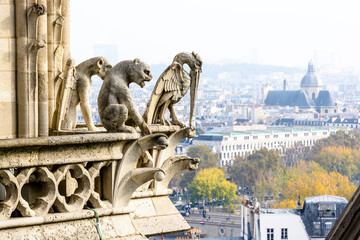 Three stone statues of chimeras on the towers gallery of Notre-Dame de Paris cathedral overlooking...