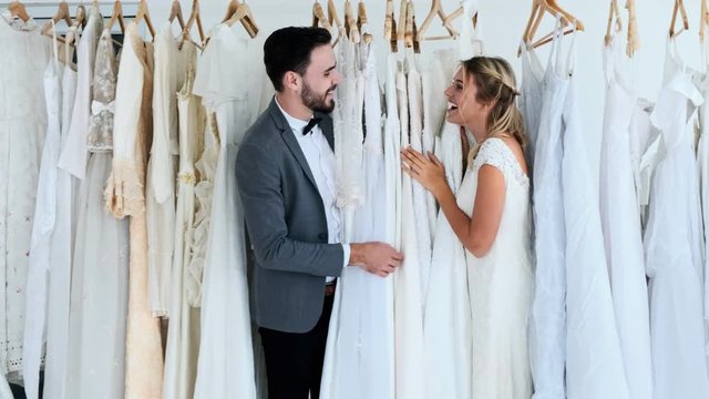 Romantic wedding couple in expensive dress shop. White man and woman in bride dress, playing hide and seek. Romantic young couple concept.