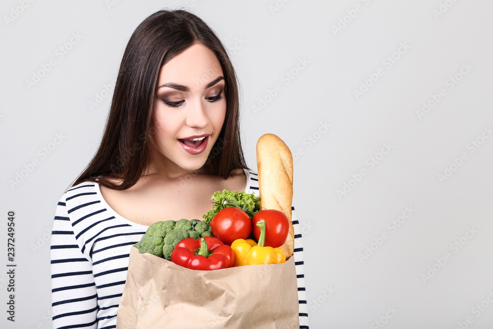 Wall mural Beautiful woman holding grocery shopping bag on grey background