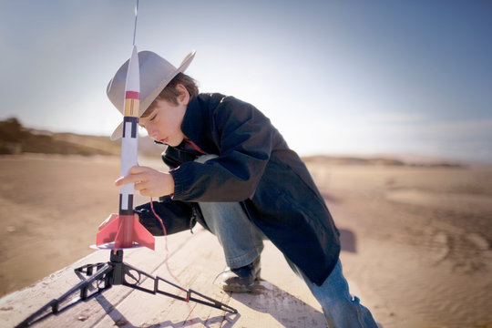 Young boy wearing a hat and putting together a toy rocket at the beach.