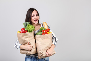 Beautiful woman holding grocery shopping bags on grey background