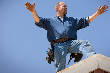 Male builder standing on the roof of a house.