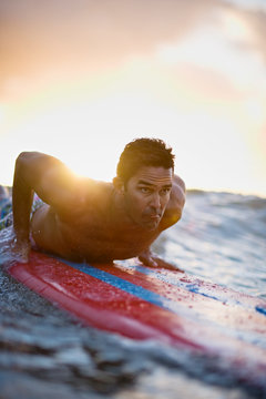 Male Surfer Prepares To Push Up Into A Standing Position As A Wave Pushes His Surfboard Forward.