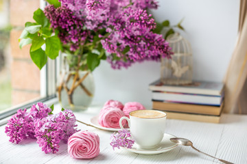 Obraz na płótnie Canvas Bouquet of lilacs, cup of coffee, homemade marshmallow and stack of books. Romantic spring morning. Selective focus