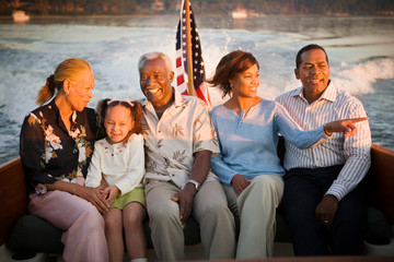 Mature adult couple sitting with a mid-adult couple and their young daughter on a boat at sunset.