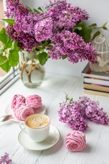 Bouquet of lilacs, cup of coffee, homemade marshmallow and stack of books. Romantic spring morning. Selective focus