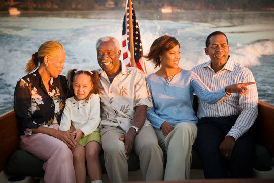 Mature adult couple sitting with a mid-adult couple and their young daughter on a boat at sunset.