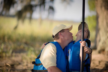 Mid-adult man trying to kiss his son's cheek as they play around with life jackets on.