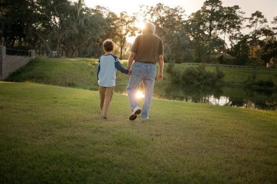 Senior adult man holding the hand of his grandson as they walk through a park.