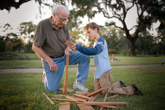 Grandfather helping his grandson to build a structure out of wood in the backyard.