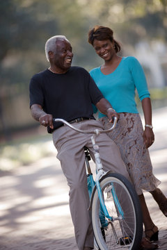 Smiling senior man sitting on a bicycle next to his mid-adult daughter.