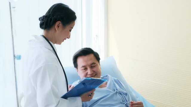 Doctor with patient. Young female medical doctor talking to a senior patient at hospital. Looking at her note to discuss medical examination result in bed. Senior care medical and insurance concept.