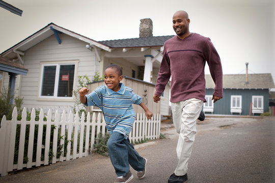 Smiling mid-adult father running down a suburban street with his young son.