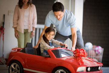 Smiling young girl sitting in a small red car given to her by her parents.