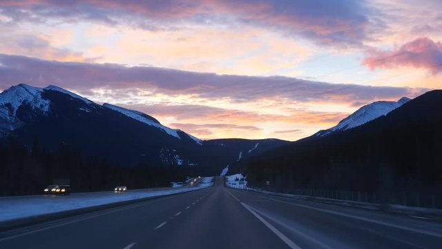 Sunrise on the TransCanada highway with snow covered Rocky Mountains. Passing traffic. Just east of the town of Canmore in Alberta, Canada.