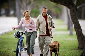 Mid-adult woman walking with a bicycle as her husband walk the dog.