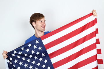 Beautiful young man holding an American flag on grey background
