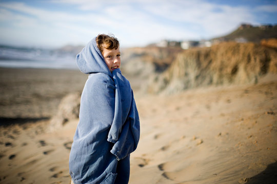 Young boy wrapped in a sweater on the beach.