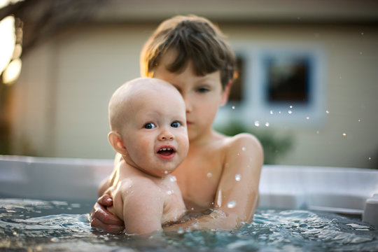 Boy holding his baby brother in a swimming pool.