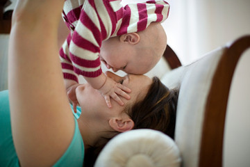 Young mother lifting her young baby in the air and touching their foreheads together.