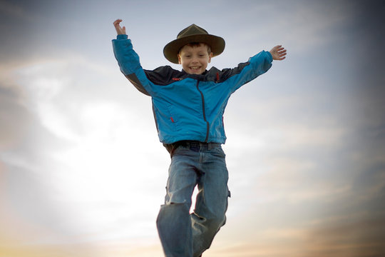 Smiling young boy jumping in the air while wearing a hat.