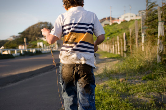 Young boy walking along a rural road with muddy jeans.