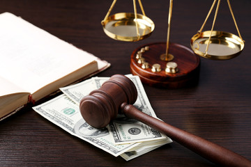Judge gavel with dollars, book and scales on wooden table