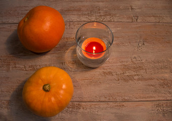 Orange pumkins with colorful candle in the glass on the wooden boards.