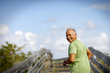 Portrait of a mature adult man smiling as he runs along a wooden beach pathway.