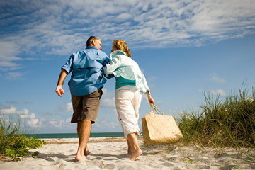 Happy mature couple holding hands while walking together at the beach.