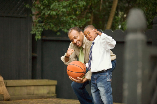 Portrait of a mid-adult man holding a basketball  with his young son.
