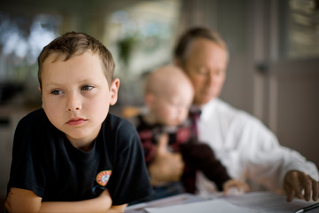 Young boy sitting with his father and younger brother.