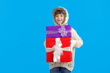 Happy little girl in winter clothes with a gift boxes in hands on a blue background. Christmas presents.