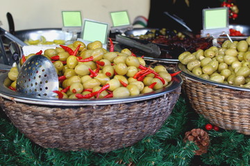 Many grenn olives with red peppers in baskets on the counter of the farmers market in the afternoon with copy space for text
