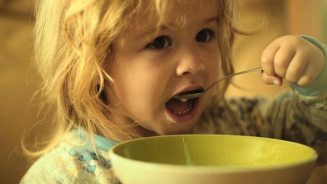 Food. A beautiful child feeds himself, eats milk porridge. Child and kitchen, healthy food. Breakfast ute boy with a spoon and a plate. Delicious food for children