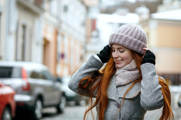 Joyful red haired girl wearing warm winter clothes walking down the street. Empty space